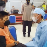 Petugas medis sedang berusaha membujuk seorang anak penyandang disabilitas supaya mau disuntik vaksin.