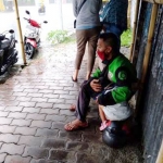 Wawan mendekap putrinya saat berteduh menunggu hujan reda, di sela pekerjaannya ojek online di Jember. Ia tetap narik ojol di tengah wabah Corona.