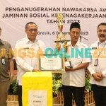 Sekdakab Gresik, Achmad Washil Miftahul Rachman, saat menyerahkan tropi kepada pemenang Nawakarsa Award Jaminan Sosial Ketenagakerjaan Desa tahun 2023. Foto: SYUHUD/BANGSAONLINE