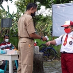 Seorang guru saat memeriksa suhu tubuh seorang siswa menggunakan thermogun. (foto: ist)