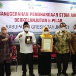 Bupati Bupati Gresik Fandi Akhmad Yani, didampingi wakilnya Aminatun Habibah, beserta sekda, ketua TP PKK, plt kadinkes, dan asisten saat menunjukkan penghargaan STBM Award 2021. foto: SYUHUD/ BANGSAONLINE