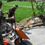 Puluhan personel TMMD imbangan mulai mengaduk campuran semen, pasir, dan batu menggunakan mesin molen.