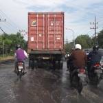 Kendaraan harus melintas pelan di jalan Raya Sukomulyo yang terendam banjir. foto: syuhud/ BANGSAONLINE