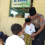 Kapolsek Senori Musa sedang membantu salah satu murid SD mengenakan sarung.