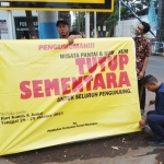 Petugas sedang memasang spanduk pemberitahuan penutupan tempat Wisata Pantai dan Kum-Kum.