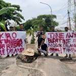 Pemuda Desa Sumberejo, Kecamatan Manyar, Kabupaten Gresik, membentangkan spanduk di tengah jalan dan sebagai bentuk protes atas jalan rusak. Foto: Ist