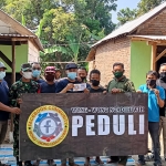 Perwakilan Divisi Peduli WWN Tomma R. Buana (pegang amplop) bersama Tim Lintas Komunitas, Perangkat Desa Kalipang, Babinsa, dan Bhabinkamtibmas di depan dua rumah Mbah Punidin (Alm) yang selesai dibedah. foto: MUJI HARJITA/ BANGSAONLINE