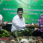 SIMBOLIS: Wabup Sidoarjo H Nur Ahmad Syaifuddin menyerahkan potongan tumpeng kepada H Mohammad Nasir Abdurrahman, kala peresmian Perpustakaan Madrasatulalsun, Sabtu (17/12). foto: mustain/ bangsaonline