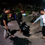 M. Syahrul Munir (kanan) menunjuk jalan rusak usai ditambal dengan aspal. (foto: SYUHUD/ BANGSAONLINE)