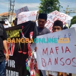 Massa aksi saat menunjukkan poster kritikan di depan pintu Kejari Sampang. Foto: MUTAMMIM/BANGSAONLINE
